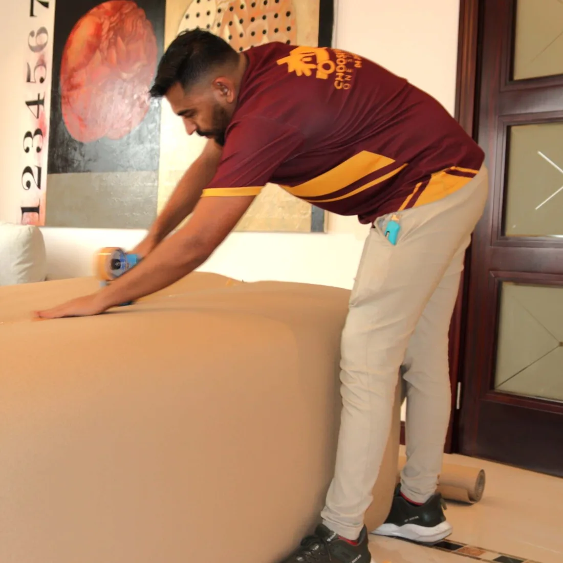 A mover wrapping a sofa in brown paper in a living room